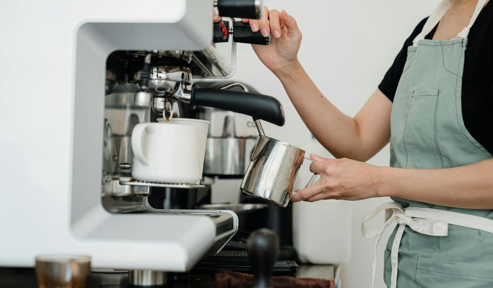 crop young woman whipping milk using professional machine in coffee shop