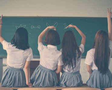 photo of four girls wearing school uniform doing hand signs