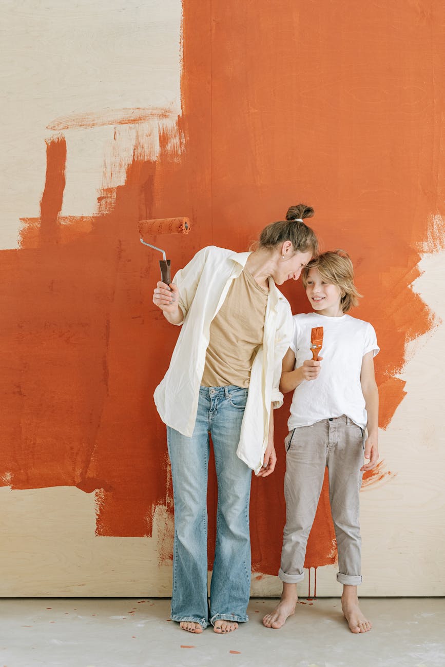 woman with a paint roller standing beside a boy holding paintbrush