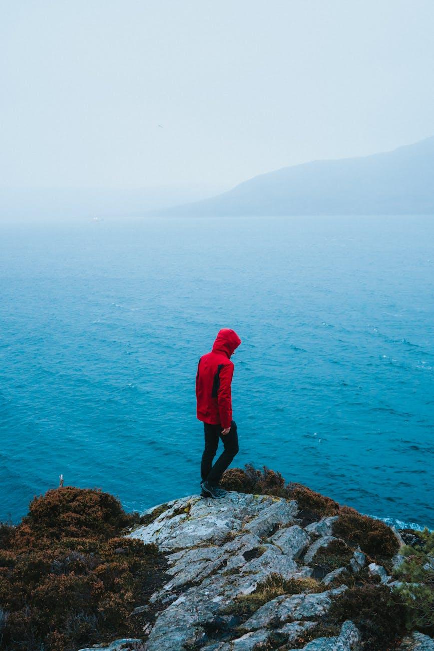 person in red jacket standing on cliff