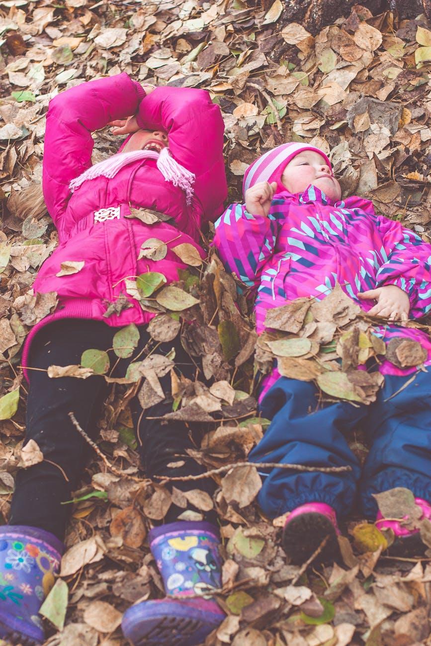 kids in pink jackets lying down on autumn leaves