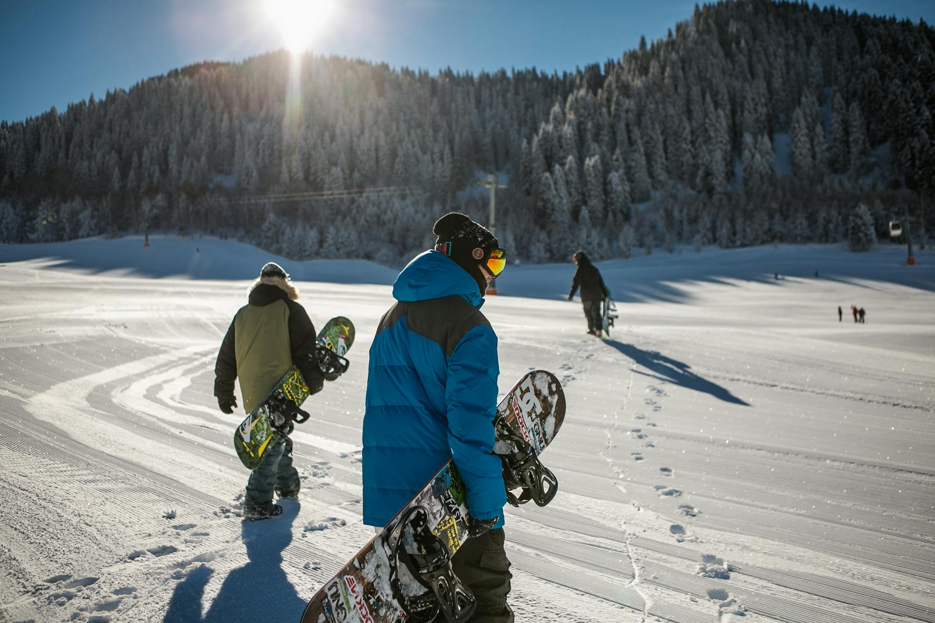 person wearing blue winter jacket carrying snowboard under sunny sky