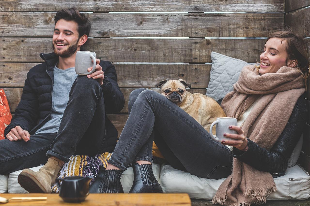 Couple sitting outside drinking coffee with a small dog on ladies lap