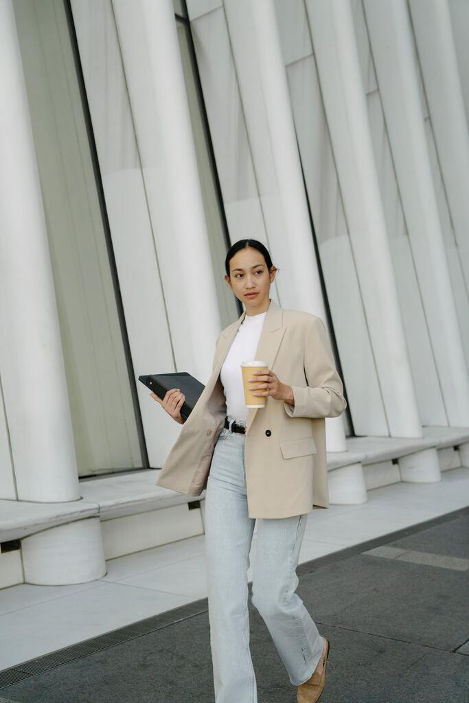 Stylish Asian businesswoman with laptop and takeaway coffee in city