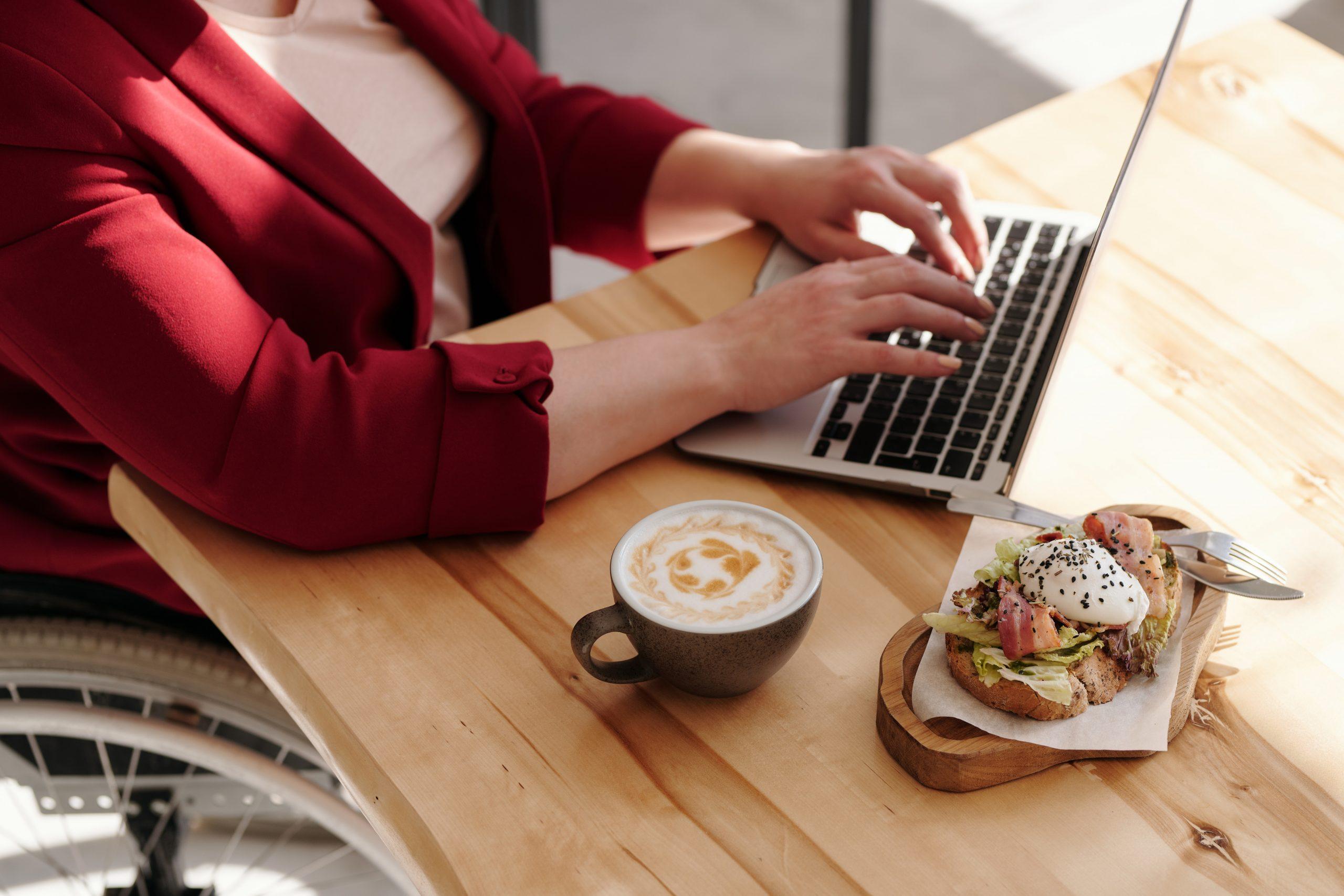 Person in red cardigan working on laptop with protein-rich snacks.