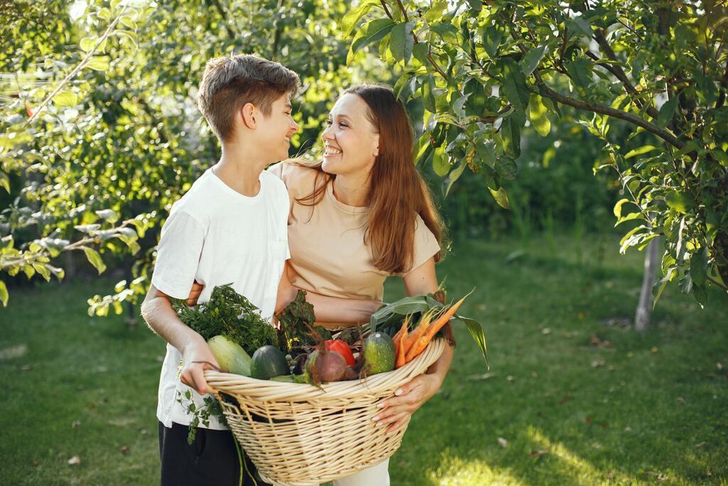 Mother and son carrying a basket full of vegetables together.