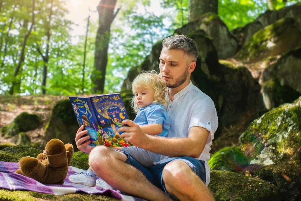 A dad reading a book to his child in a park.