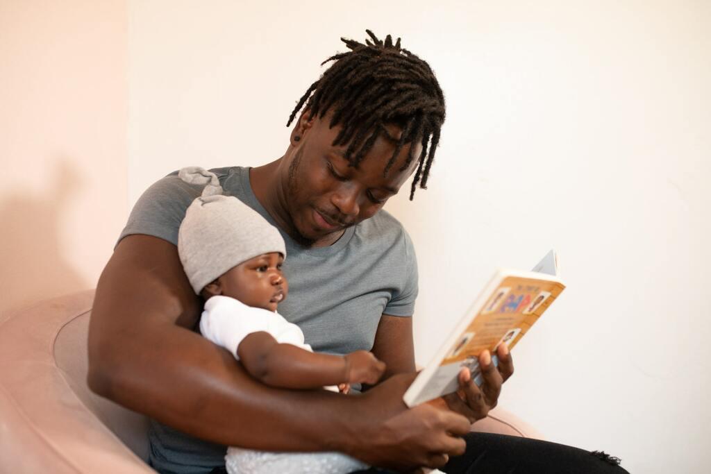 A father reading a book with his baby in his arms.