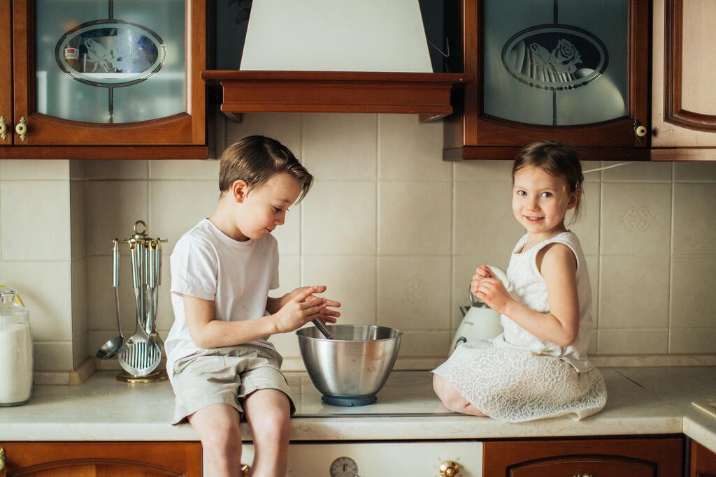 A brother and a sister playing in the kitchen.