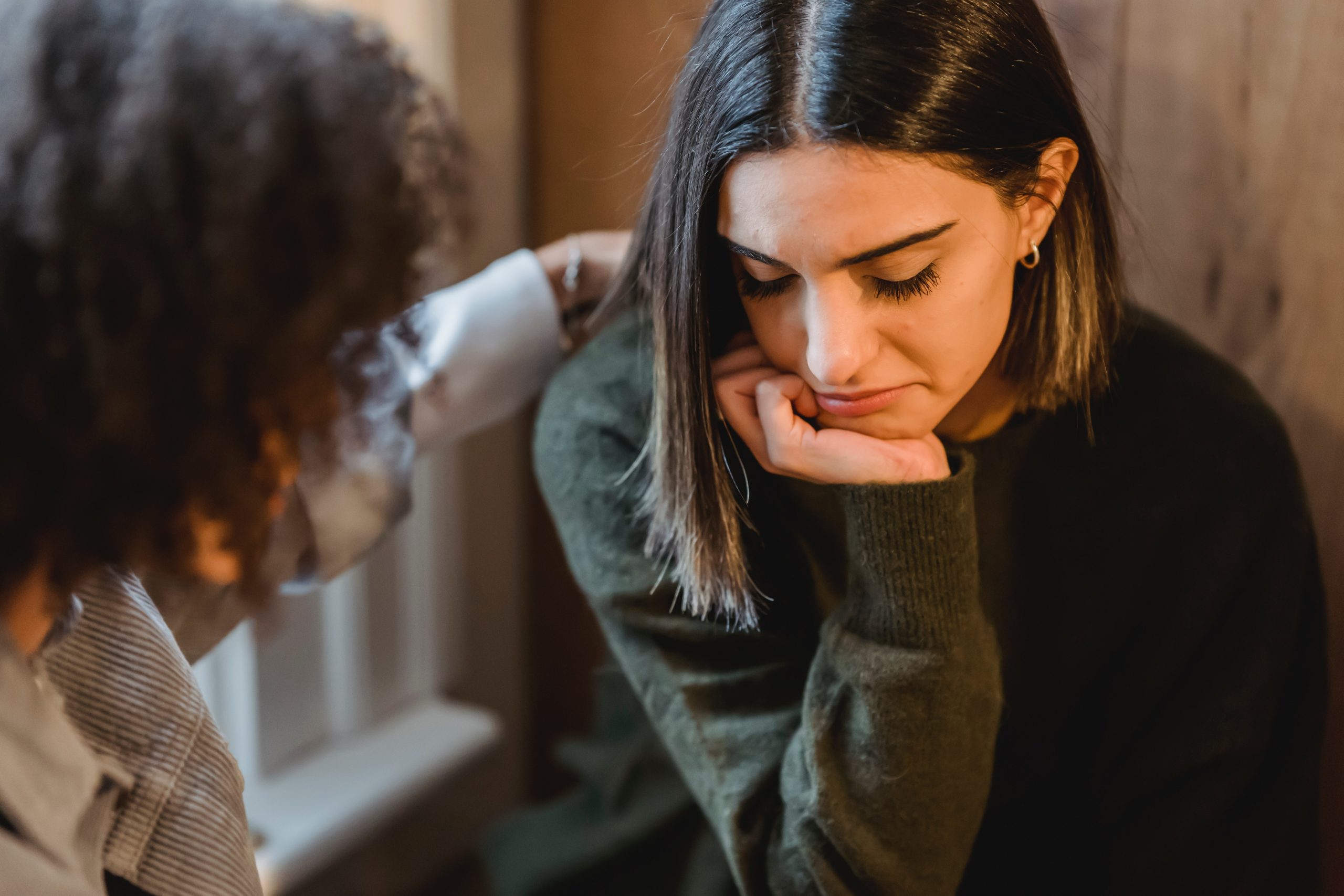 Crop woman tapping shoulder of emotional female friend