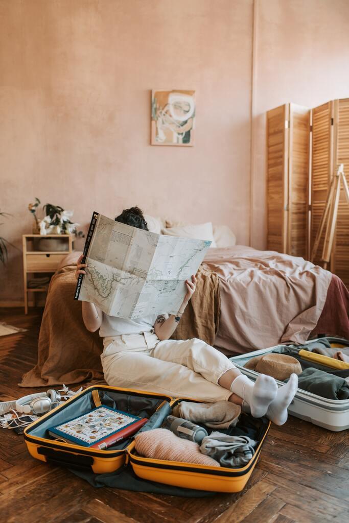 Person in White Pants sitting on floor reading a road map surrounded by suitcases.