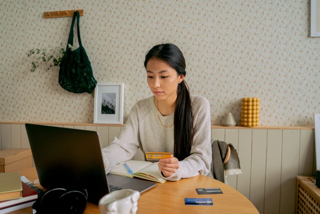 Woman in grey sweatshirt shopping online with credit cards.