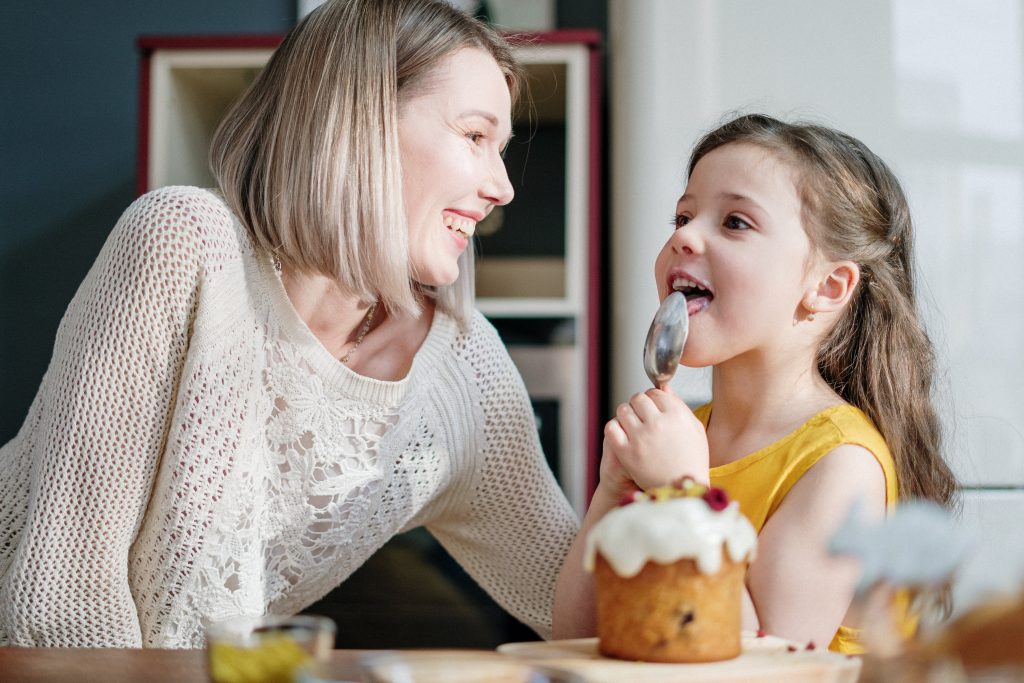 Mother and daughter making cakes, while daughter licks the spoon