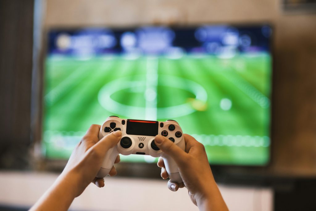 A person holding a games console controller in front of a television