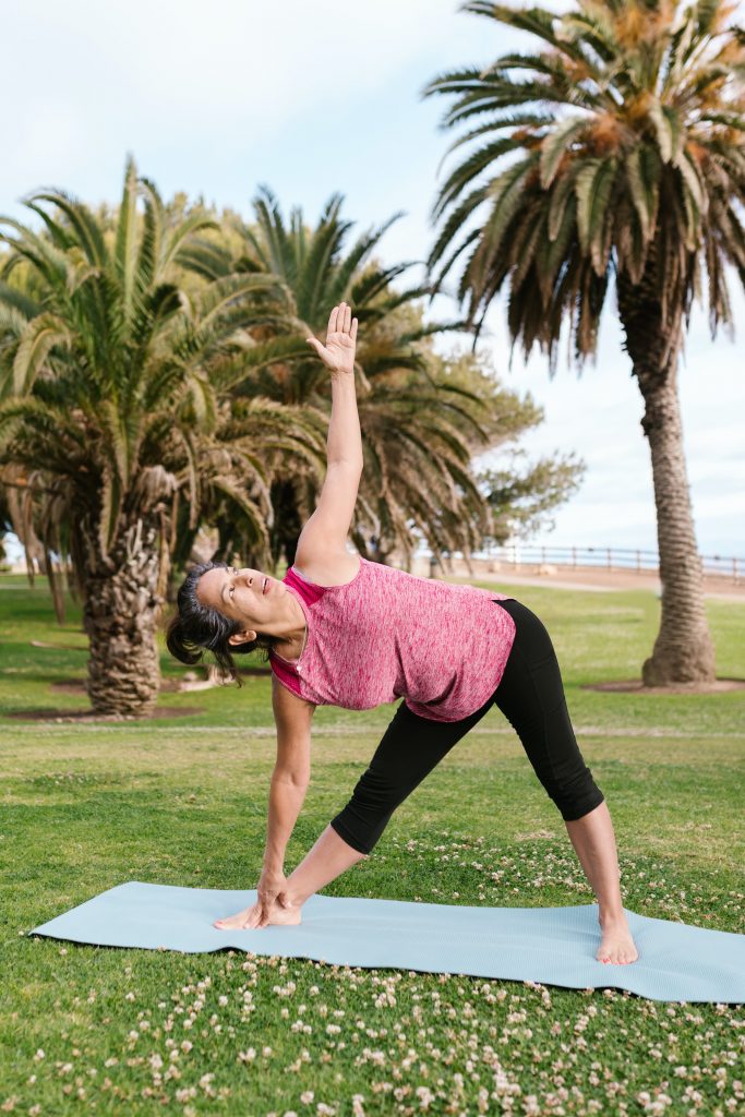 Elderly lady in pink top doing yoga on blue mat in front of beach