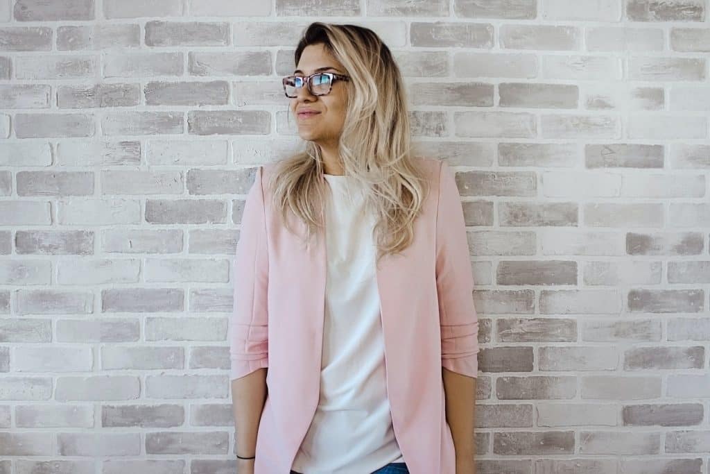 Woman in pink jacket leaning against a wall.