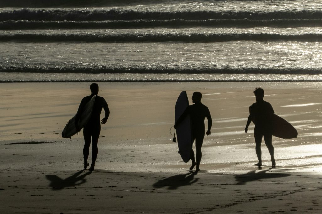 Three persons carrying surfboards in Newquay