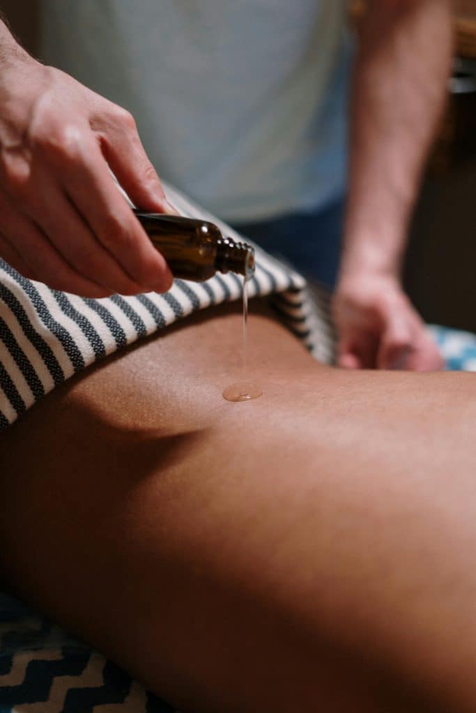 Person Holding Black and White Stripe Textile pouring oil onto back of someone