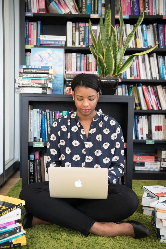 Woman Sits on Floor Facing Gold Macbook researching