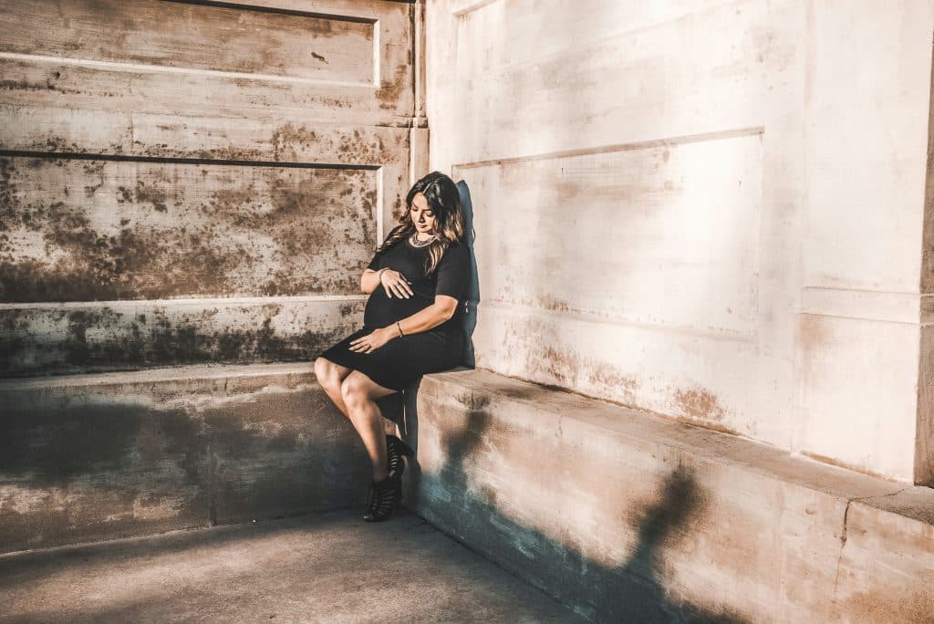 woman sitting on concrete wall cradling her baby bump