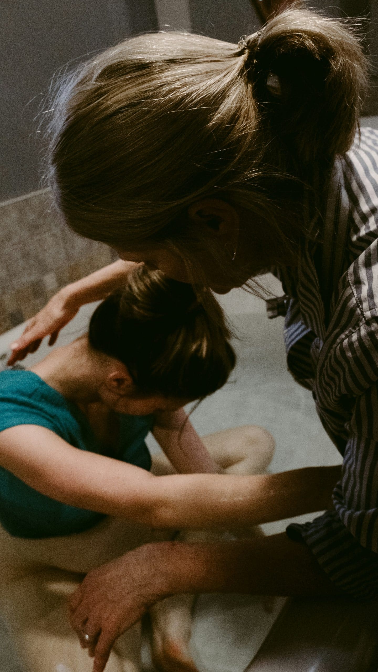Woman sitting in birthing pool being assisted by midwife