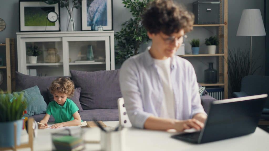 Mother Working on Laptop and Son Playing behind