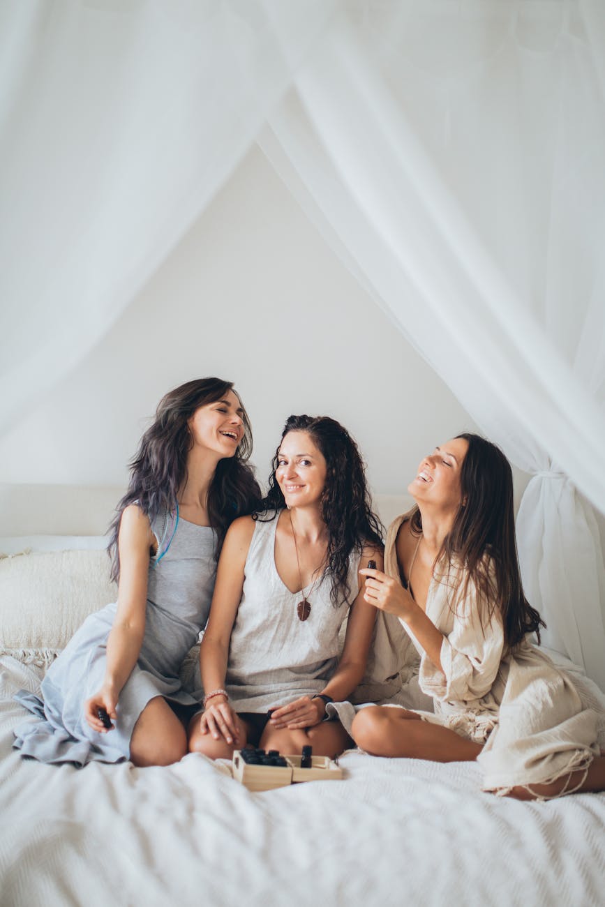 a group of beautiful women sitting on the bed while having fun