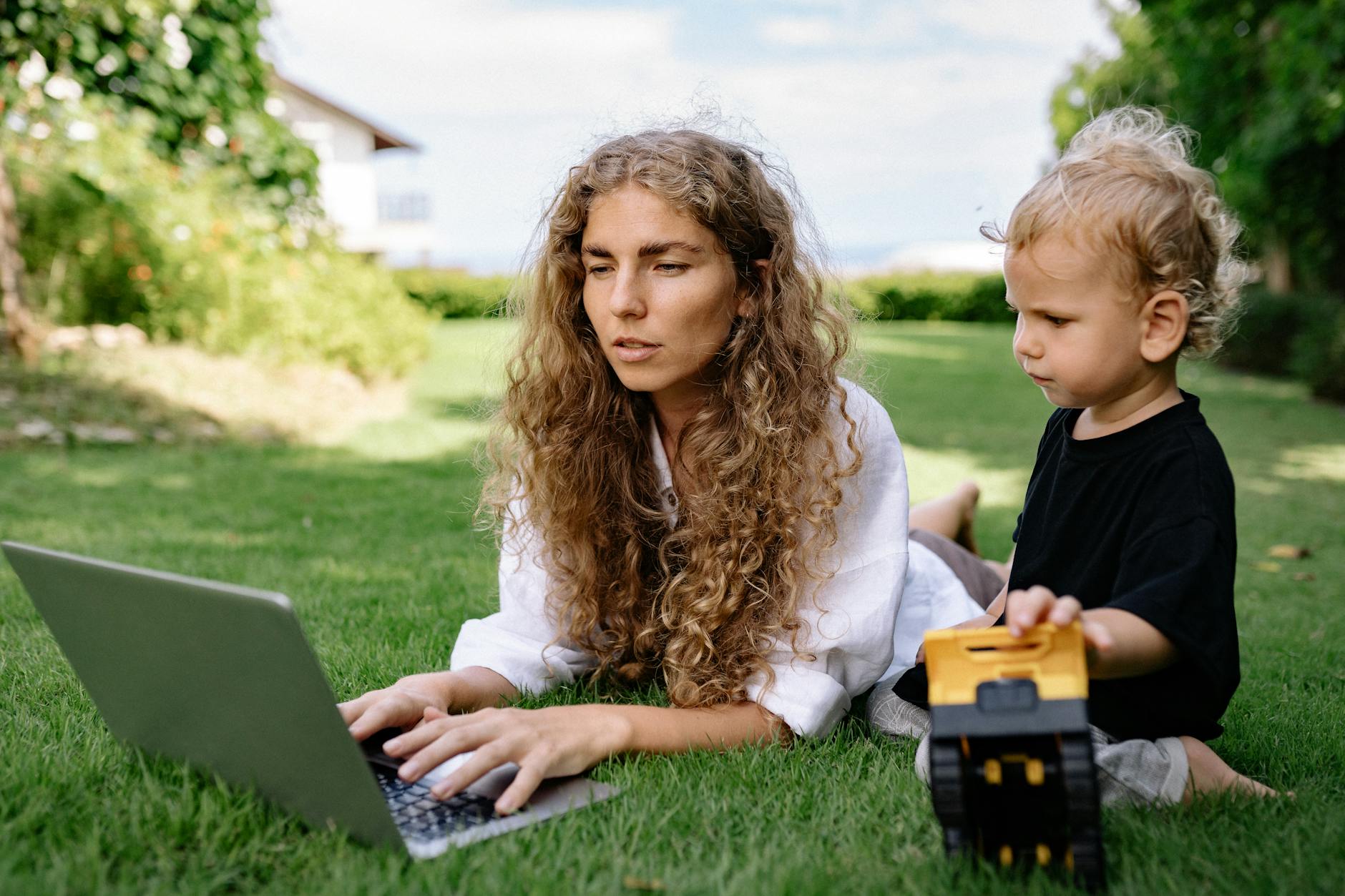 photo of woman using silver laptop while lying on grass field