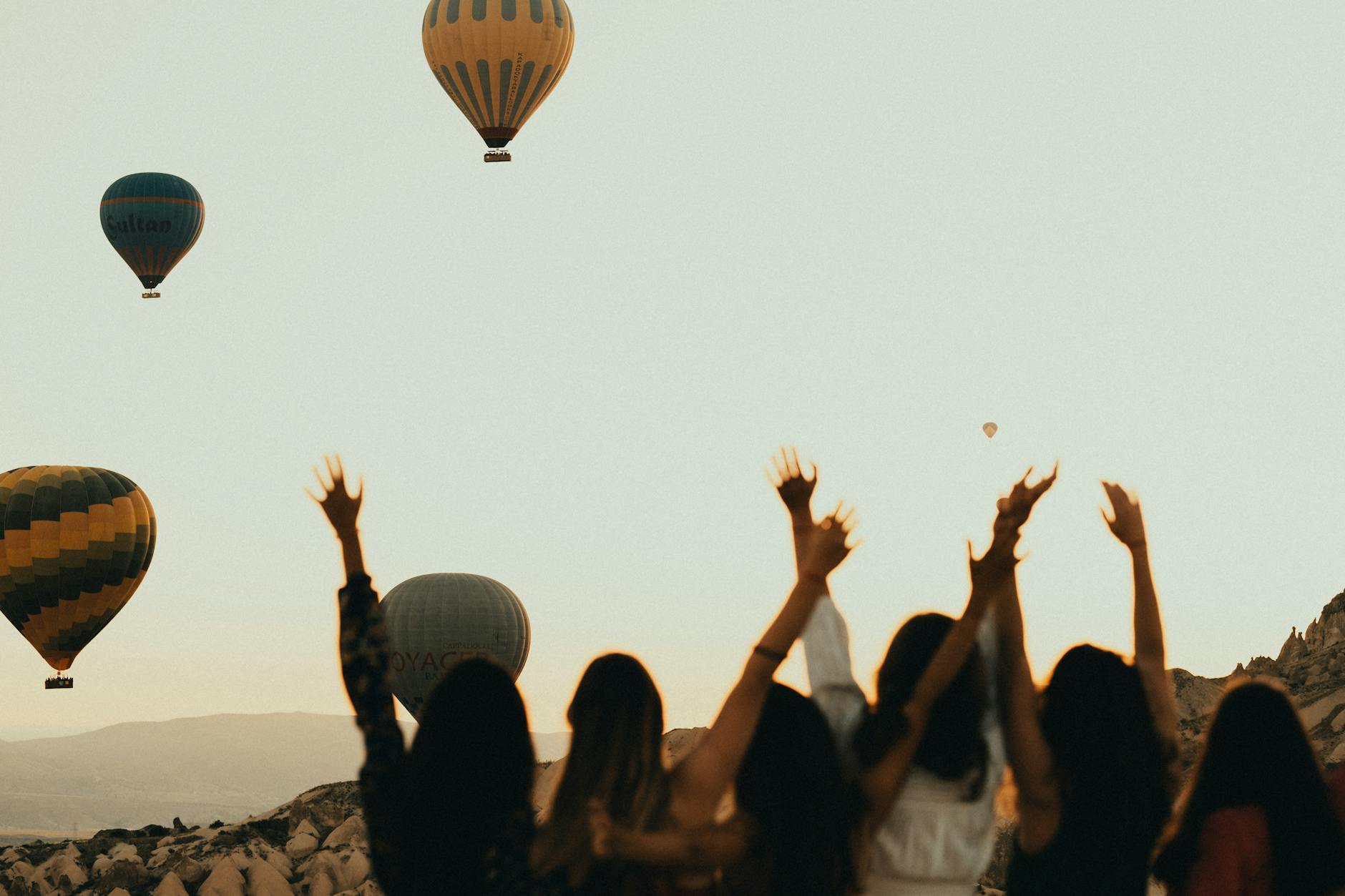women with their arms raised watching hot air balloons