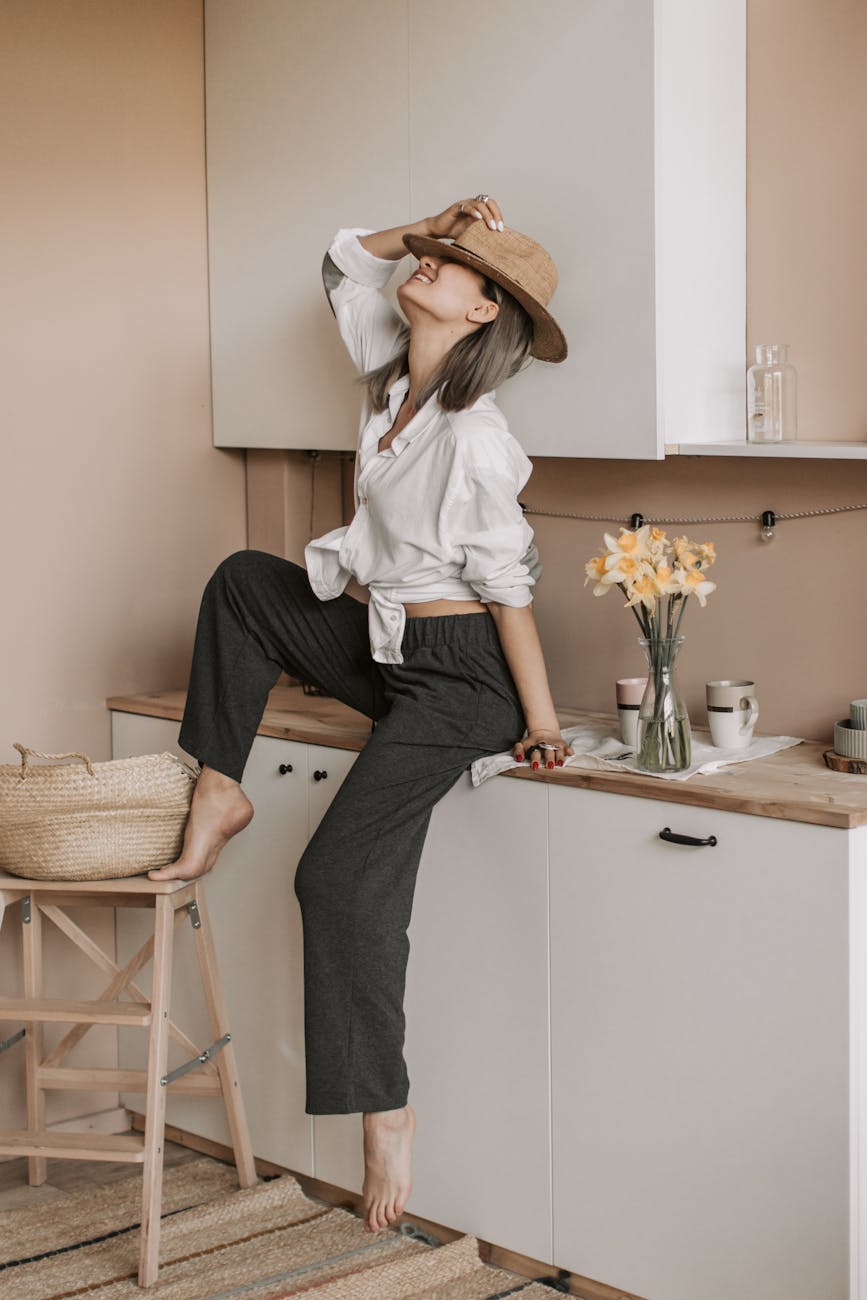 woman holding her hat while sitting on a cabinet