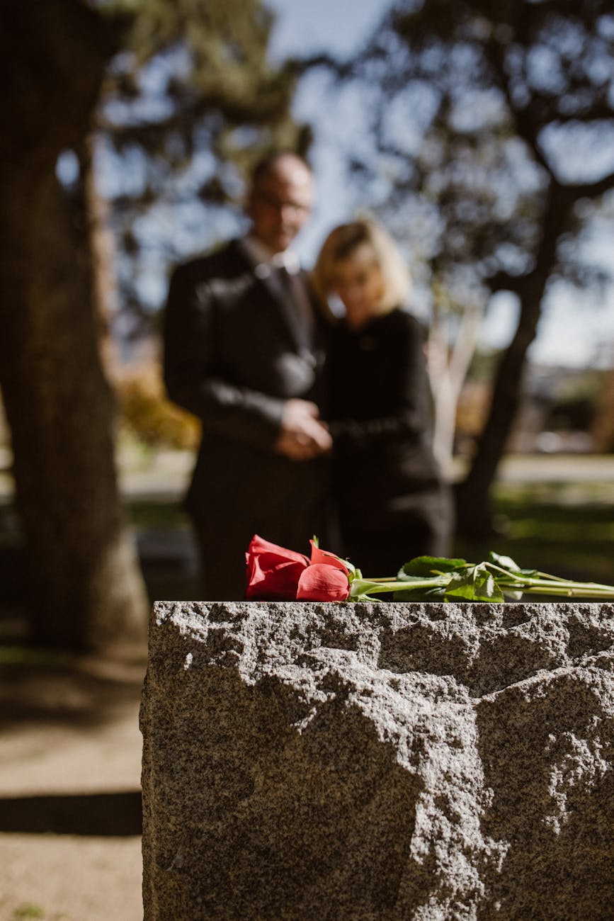 man and woman standing on grave with flower on tombstone