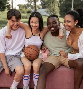 Happy multiracial friends embracing on bench after basketball training