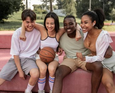 Happy multiracial friends embracing on bench after basketball training