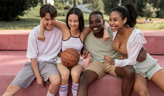 Happy multiracial friends embracing on bench after basketball training
